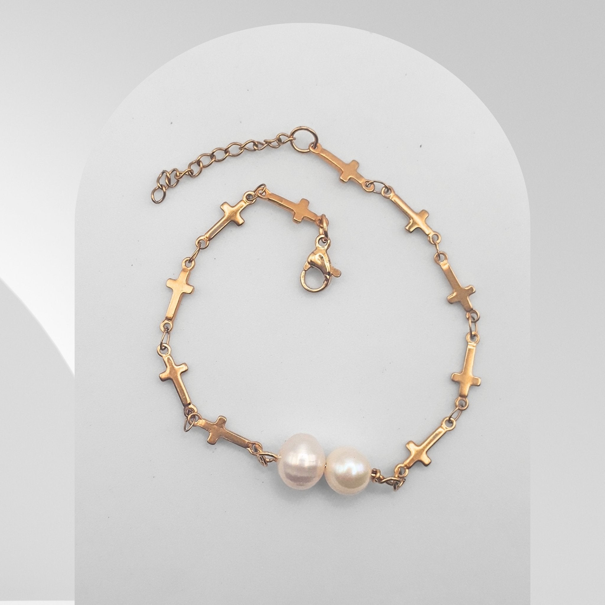 Gold bracelet with cross designs and pearls on a light gray background