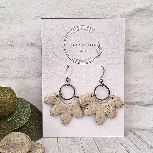 These handmade earrings feature a unique shape crafted from polymer clay in a beautiful cream color with little black spots
