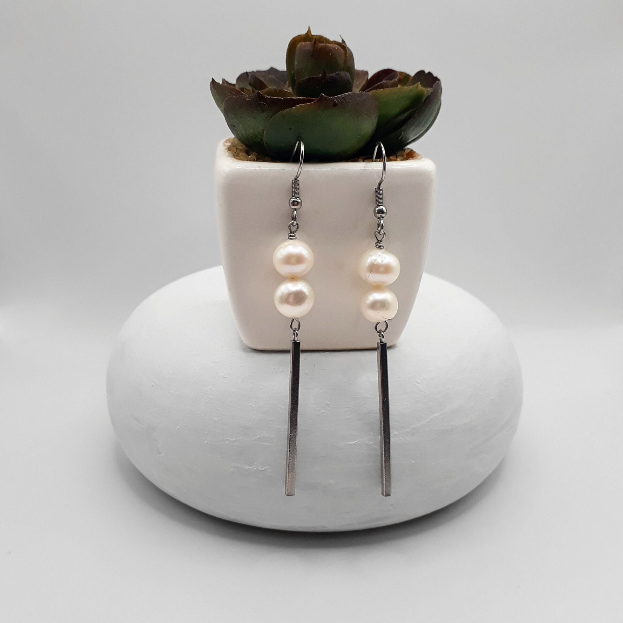 White natural freshwater pearl dangle earrings with stainless steel bar drops displayed against a minimalist background.