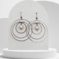 Pair of earrings with circular design and pearl-like beads on a white stand.