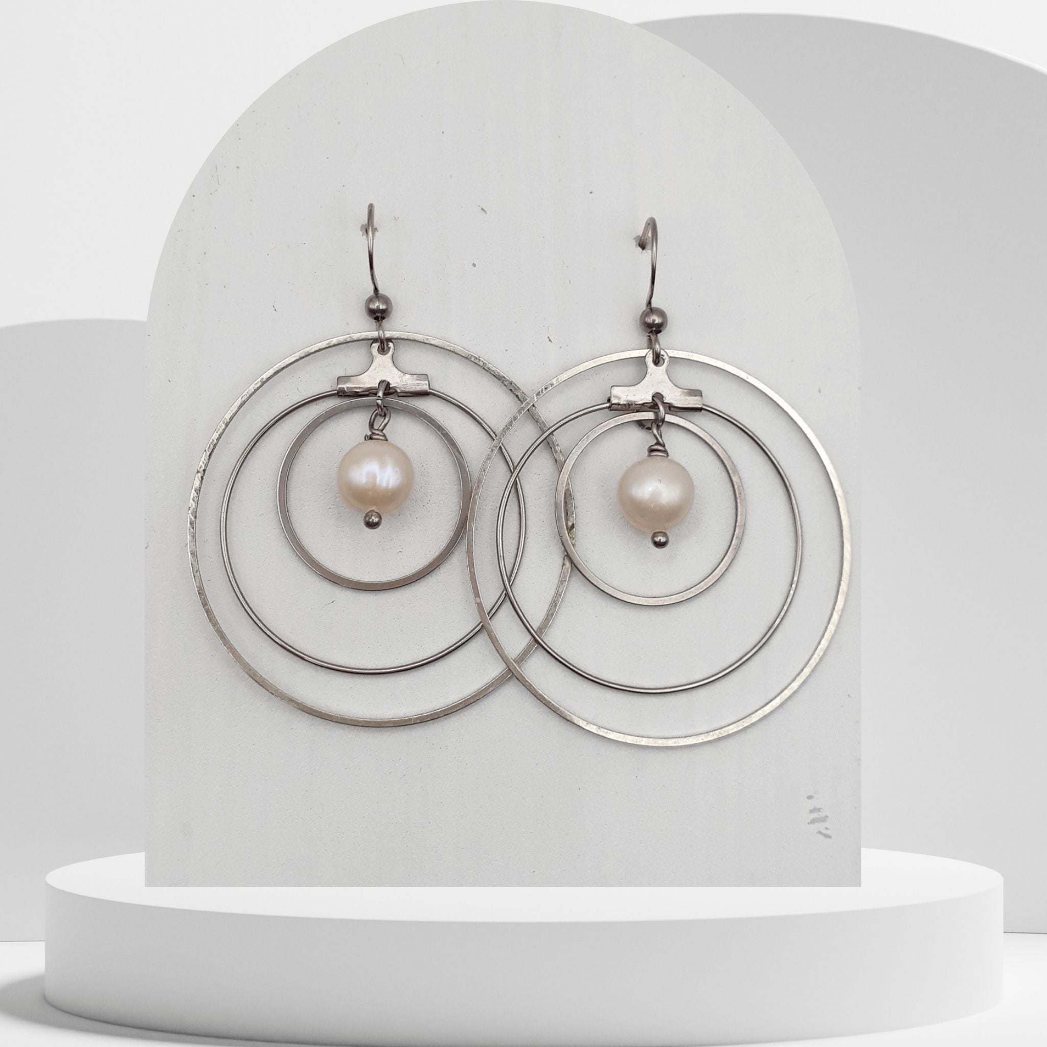 Pair of earrings with circular design and pearl-like beads on a white stand.